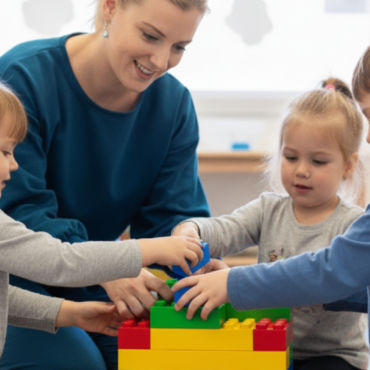 Smiling woman and three young children building with colourful blocks on a playmat during a social skills support session